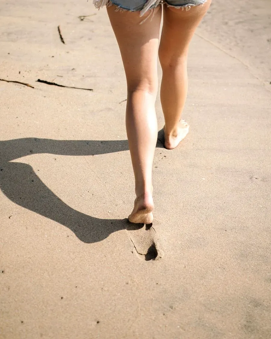 Pernas de mulher caminhando descalça na areia