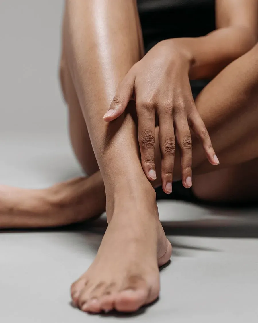 Mulher sentada tocando as pernas de pele firme